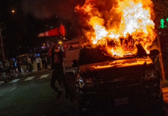 미국 백악관에서 한 블록 떨어진 워싱턴의 한 도로에서 지난달 30일(현지시간) 흑인 남성 조지 플로이드의 사망에 항의하는 시위가 벌어진 가운데 한 시위 가담자가 불타는 차량에 원뿔형 교통표지판을 던지고 있다. 사진=연합뉴스.